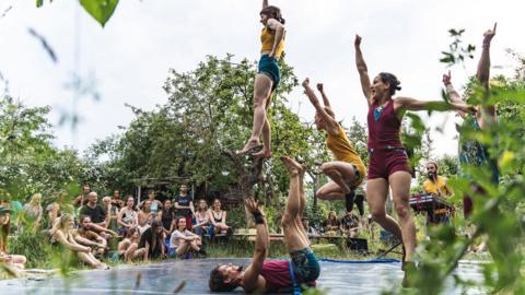 People jumping in the air during an outdoor aerobic exercise class, watched by an audience