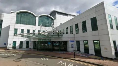 A white hospital building with No Parking signes written on the ground outside the main entrance