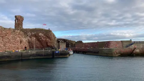 Dunbar RNLI Dunbar Harbour which has stone walls and steep rocks on one side.