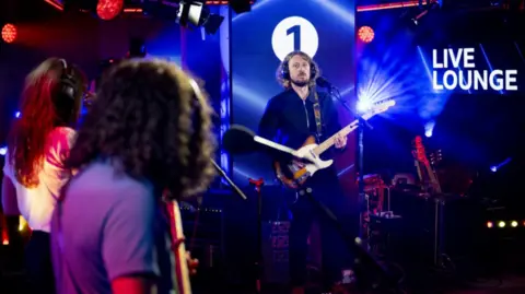 The Zutons performing in a BBC studio with the lead singer playing a guitar accompanied by other band members