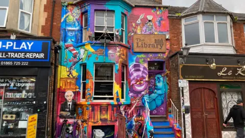 The Library pub with a very colourful mural on its whole facade, including the Cheshire Cat from Lewis Carroll's Alice's Adventures in Wonderland, author Colin Dexter's Inspector Morse and Gandalf from JRR Tolkien's Lord of the Rings