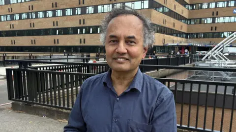 Professor Guru Aithal stood outside Nottingham's Queen's Medical Centre wearing a blue shirt