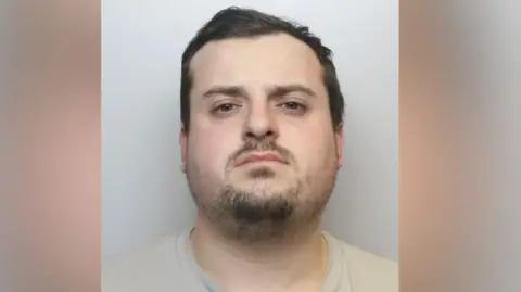 A police mugshot of a Joshua Martin, a man in his twenties with short dark hair and stubble. 