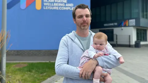 David Lewis holding his baby outside the Blair Mayne leisure centre