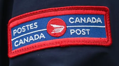 Um distintivo azul e vermelho próximo em um uniforme azul azul com o logotipo do Canadá em francês e inglês via Gotti Images via Bloomberg. 
