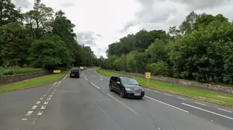 Streetview image of a busy rural road with trees on both sides