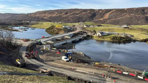 Highland Council The new Naver Bridge, whilst construction works were still underway. A small crane can be seen on the road leading up to the bridge. It's a sunny day, with hills in the background.