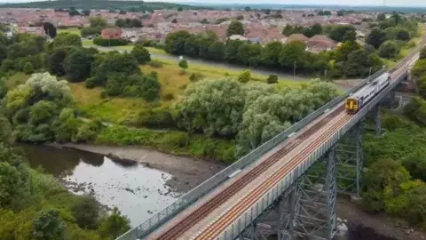 Northern A train made up of two carriages cross a railway viaduct. Behind it you can see a large town. 