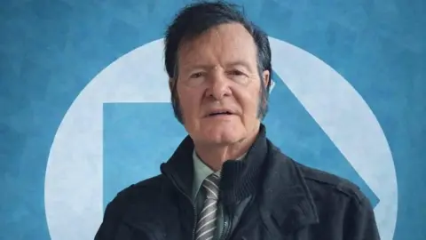 Victor Hagan has dark black hair and wears a green shirt and striped tie in this Reform Party profile