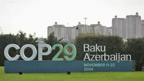 Reuters A sign announcing the COP29 United Nations Climate Change Conference November 11-22 2024, against a backdrop of white multi-storey apartment buildings 