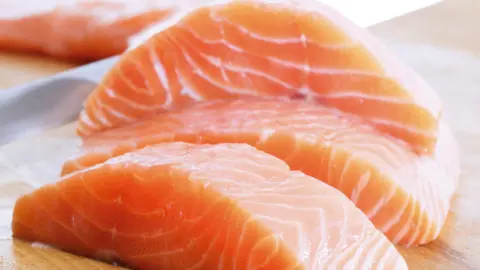 Close-up shot of three salmon fillets on a wooden counter top with blurred background