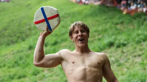 Reuters Tom Kopke, from Munich, holds a cheese wheel after winning the annual Cooper's Hill Cheese-Rolling and Wake competition near Brockworth. 