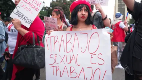 Women march in a rally holding up signs which say: “Sex work is work” and “I am a sex worker”.