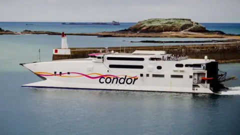 Getty Images A ferry - small, white vessel with Condor written on the side with two pink and orange wavy lines - near a dock with an island in the background