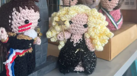 Two knitted figures - one as a fairy godmother, the other Adam Ant, a scene from a music video