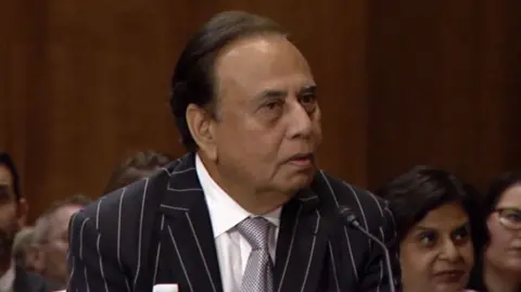 Anjani Sinha is wearing a black and white pinstripe jacket, grey tie and white shirt