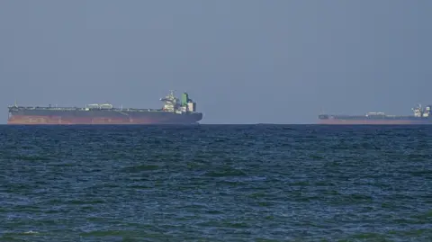 A generic image of vessels in the Strait of Hormuz. Two cargo ships upon the horizon, water in the foreground.
