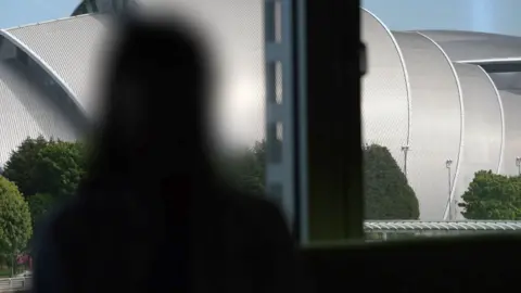 Blurred silhouette of "Alice" with Glasgow's Armadillo venue outside the window