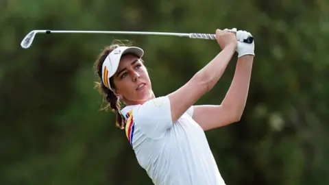 PA Georgia Hall wearing white and swinging a golf club.