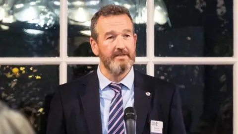 Cabot Learning Federation Steve Taylor wearing a dark blue suit speaking into a microphone 