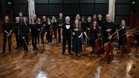 Paul Leonard-Morgan An orchestra standing up in a recording studio. Among them are Paul Leonard-Morgan and Len Pennie.