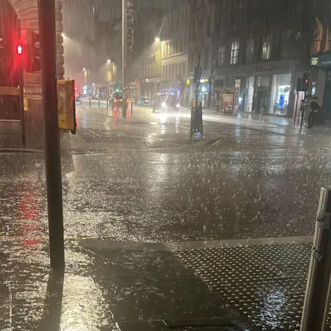 Peter Burr Glasgow city centre street at night, dark, with rain battering off the ground.