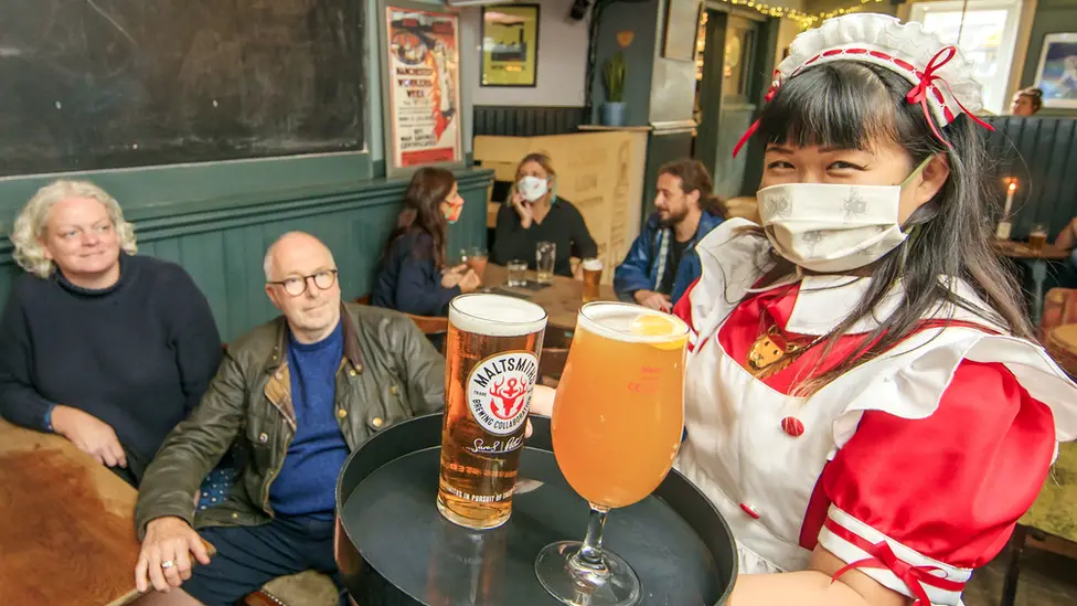 PA Media Woman in mask serves drinks to pub customers
