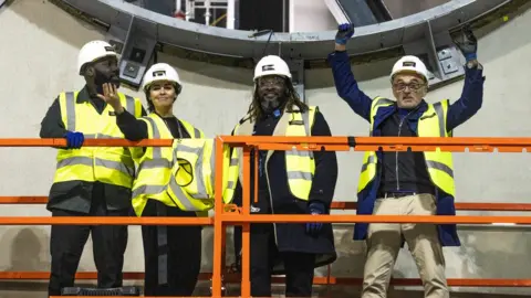 PA Media Danny Boyle (right) and collaborators Michael Asante, Es Devlin and Kenrick Sandy in the under-construction Factory International