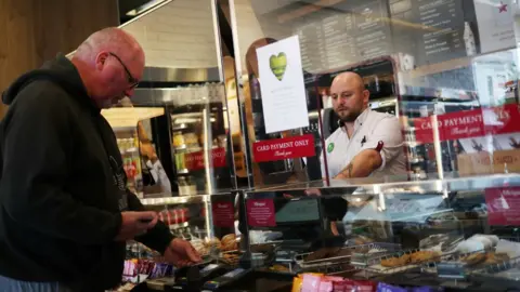 Reuters An employee is seen behind a protective screen as they serve a customer in a Pret a Manger store that has reopened for delivery and takeaway in Wimbledon on 1 May