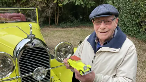 Justin Dealey/BBC Malcolm Stern in front of his father's 1930's classic car holding a model of the car