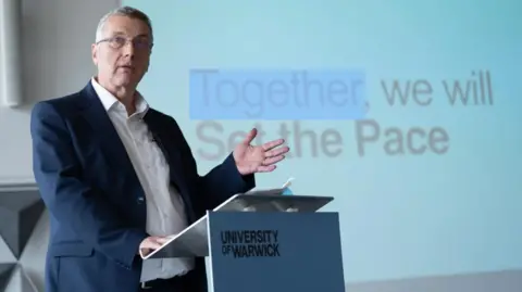 A male professor standing at a podium delivering a presentation in a lecture room