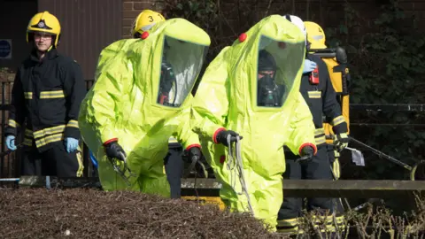 Empics Specialist officers in protective suits prepare to secure the police forensic tent that had been blown over by the wind and is covering the bench where Sergei Skripal was found critically with his daughter on March 4