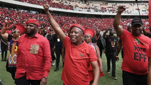 Getty Images Julius Malema, leader of the Economic Freedom Fighters (EFF), centre, salutes the crowd during the Economic Freedom Fighters party manifesto launch in Durban, South Africa, on Saturday, Feb. 10, 2024