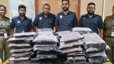 Susitha Fernando Six Sri Lankan officials stand over bags sealed up, stuffed full of drugs, were found in two large suitcases