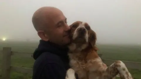 Martin Heath/BBC Man with bald head cuddles brown and white dog