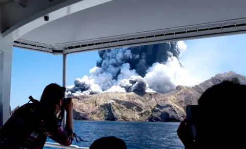 Michael Schade / Twitter Tourists on a boat witnessing and taking photos of the volcano on New Zealand's White Island as it spews steam and ash