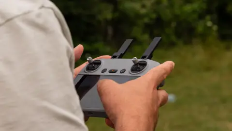 Getty Images Person's hands holding and using a drone remote controller with joysticks in an outdoor setting.