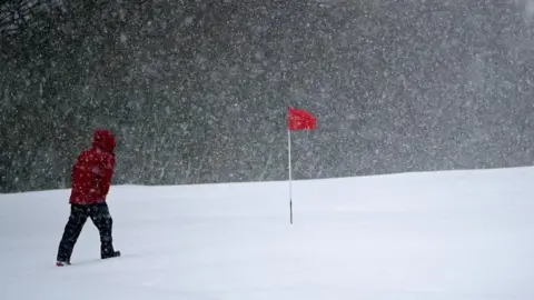 PA Media A man walking over a golf course in heavy snow