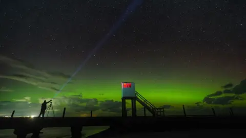 Owen Humphreys/PA Media A show of the Northern lights over the refuge hut on the Holy Island causeway in Northumberland