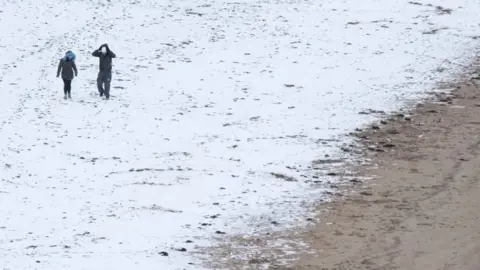 Getty Images A couple walk through snow along the beach in the sea side resort of Scarborough in North Yorkshire