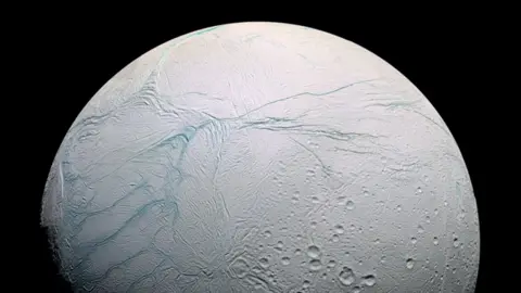 NASA Image of a white ice moon with blue lines streaked across its surface and a small cluster of craters
