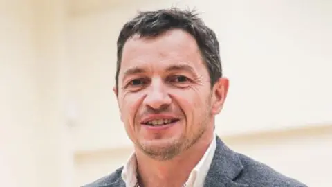 Geraint Evans in white shirt and grey blazer, smiling at the camera