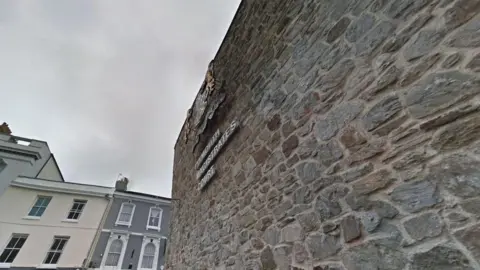 A large brick wall with Plymouth Magistrates' Court written on the side with the court's emblem above. 