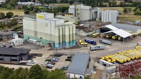 Ant Saddington/BBC A drone shot of a mill, with lots of vehicles around it, large containers, with grass in the distance. 