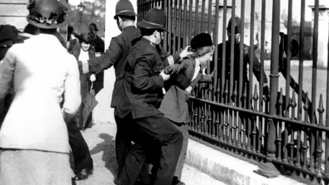 PA Demonstrator being restrained by police during a suffragettes gathering outside Buckingham Palace on 21 May 1914