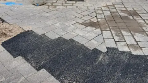 Black tarmac fills the gaps in the pavement, with the original grey paving stones surrounding it.