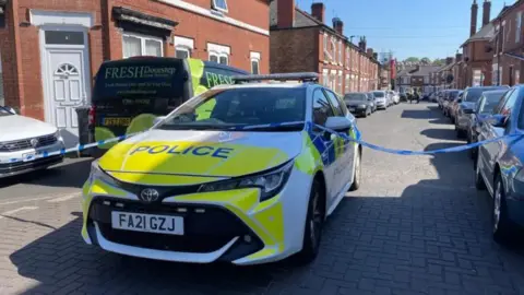 A police car with police tape on a road with terraced houses at either side