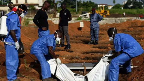 AFP Health workers from the Sierra Leone's Red Cross Society Burial Team 7 place a body in a grave at King Tom cemetary in Freetown on November 12, 2014