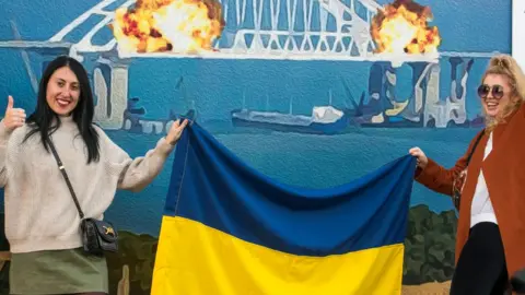 EPA Two women pose with the Ukrainian flag in front of the artwork in central Kyiv, Ukraine