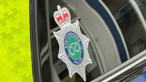 The side of a police vehicle, with a crest of Staffordshire Police in the corner of the window